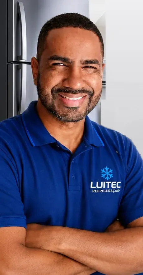 Luiz, da Luitec Refrigeração, de camisa polo azul com a logo, de braços cruzados, com uma geladeira ao fundo